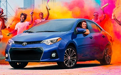 image of a blue Toyota driving through colorful smoke with people 